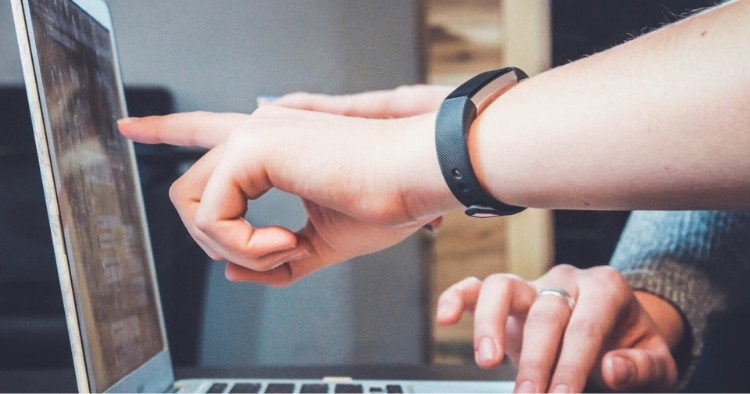 Two people sitting at a computer, one showing the other something on it representing training in the workplace