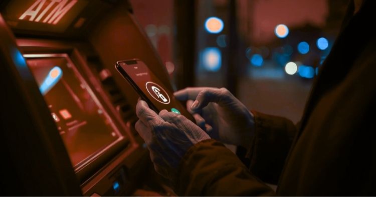 Elderly person holding a smartphone near an ATM, representing bank impersonation scams targeting seniors