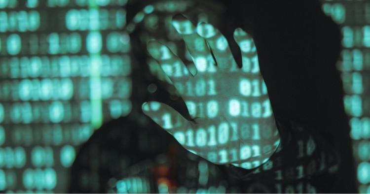 Man standing in front of a projector that is projecting a binary code that the man is being consumed by, holding his hand in front of his face