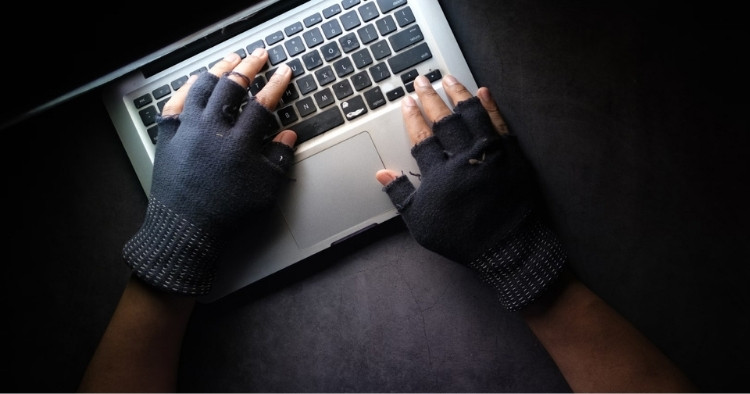 Hands typing on a laptop with gloves with the fingertips cutoff, most likely a criminal