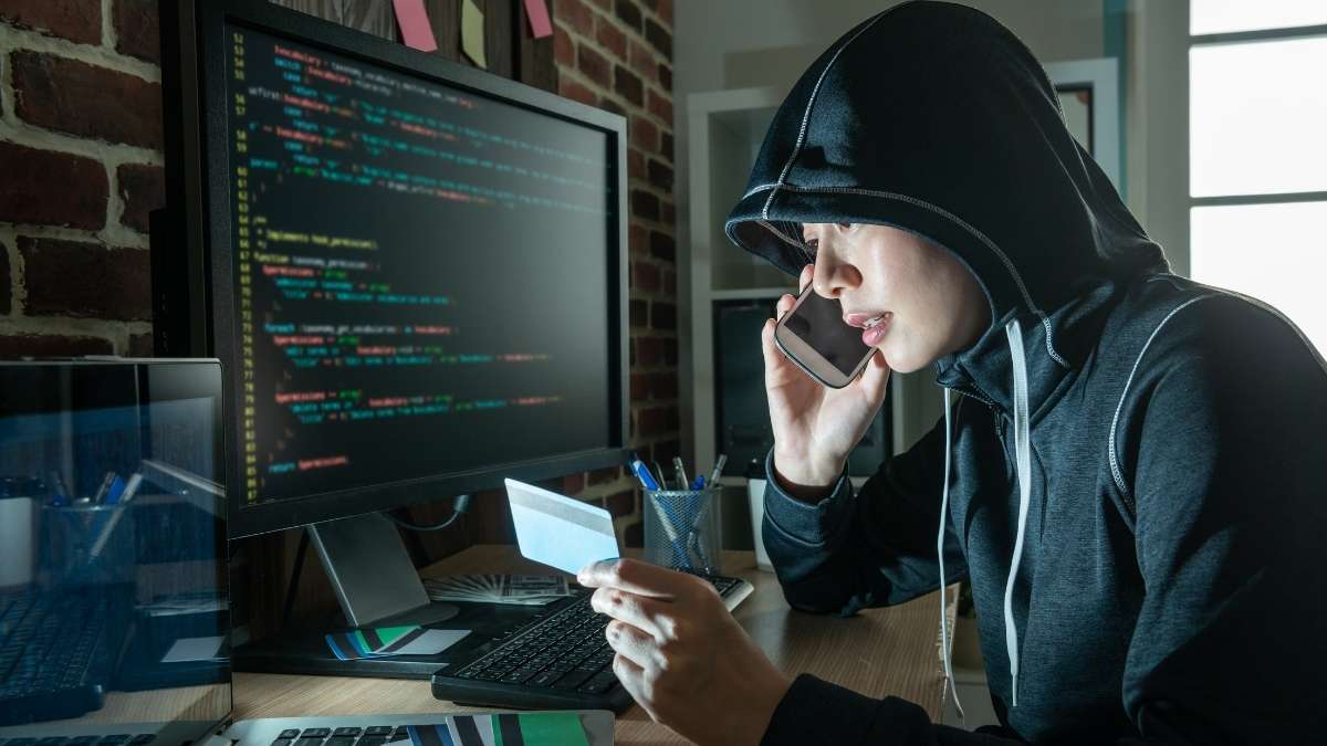 Young man with hoodie at a computer with a credit card, ready to purchase Ransomware as a Service (RaaS) online