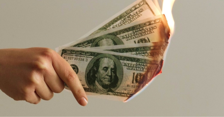 Four one hundred dollar bills burning while someone is holding it representing businesses losing money due to breaches