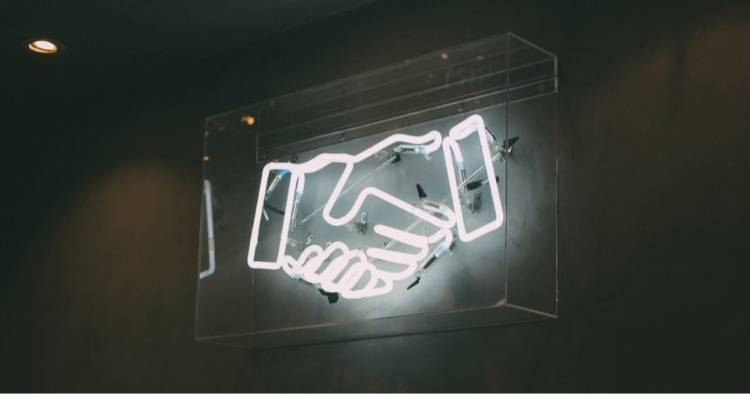 Neon white sign of hands shaking in a clear box representing the ongoing partnership between STACK and our vendors